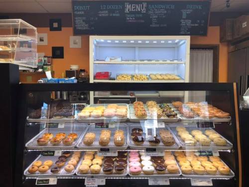 A display case filled with various donuts, including glazed, chocolate, and colorful options, in a cozy shop setting.