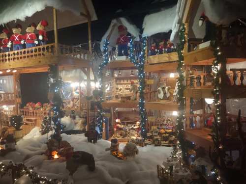 A festive display featuring wooden toy soldiers, decorated houses, and holiday lights amidst a snowy scene.