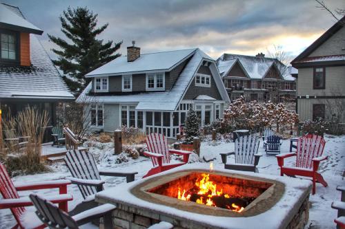 A cozy winter scene featuring a fire pit surrounded by colorful chairs, with snow-covered houses in the background.