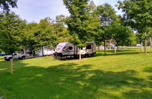 A parked RV surrounded by green trees and grass in a scenic outdoor area.