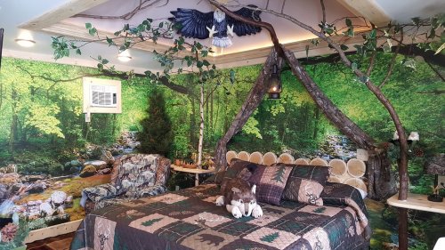 Cozy woodland-themed bedroom with a nature mural, log furniture, and a quilt featuring animal patterns.