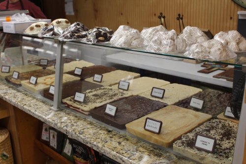 A display case filled with various types of fudge and confections, labeled and arranged on a granite countertop.