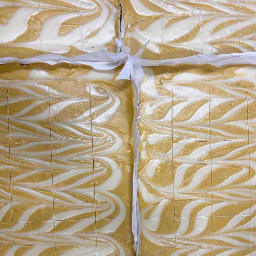 A close-up of a creamy, swirled dessert with golden and white layers, neatly cut into squares and tied with a ribbon.