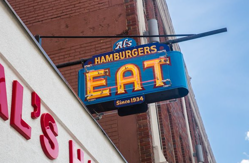 A vintage neon sign reading "Al's Hamburgers EAT Since 1934" against a brick wall.