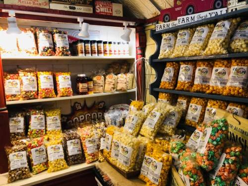 A colorful display of various popcorn flavors in bags and jars on shelves in a cozy shop.