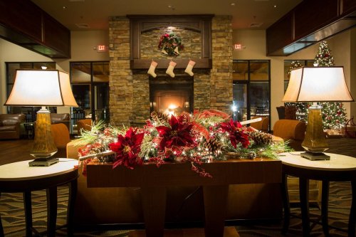 A cozy lobby decorated for Christmas, featuring a fireplace, stockings, and festive floral arrangements.