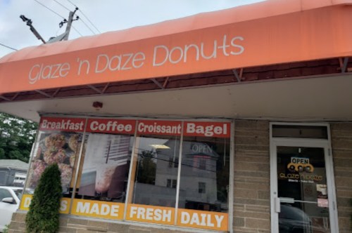Exterior of Glaze 'n Daze Donuts shop with an orange awning, featuring signs for breakfast, coffee, and fresh donuts.