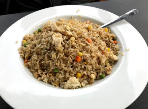 A plate of fried rice with chicken, mixed vegetables, and a fork on the side.