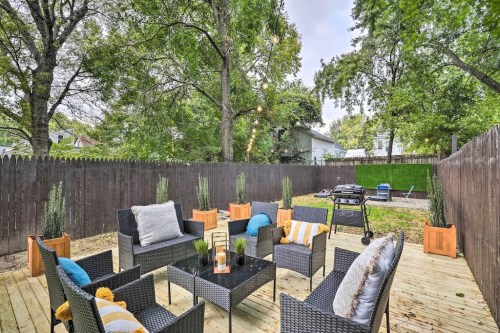 Cozy outdoor patio with seating, potted plants, and a grill, surrounded by trees and a wooden fence.