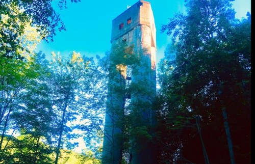 A tall, weathered concrete tower surrounded by lush green trees under a bright blue sky.