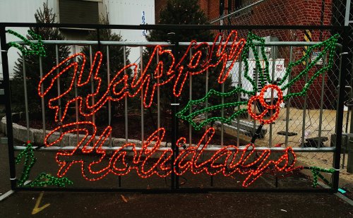 A festive display reads "Happy Holidays" in bright lights, surrounded by holly leaves and berries.