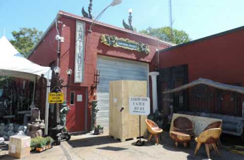 A vintage shop entrance with a wooden door, antique furniture outside, and a sign indicating "Arrowmika Enter Here."