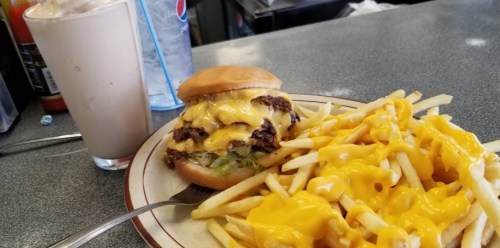 A plate with a cheeseburger topped with melted cheese, lettuce, and a side of cheesy fries, alongside a milkshake.