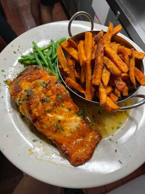 A plate featuring grilled salmon with a glaze, served with green beans and a side of crispy sweet potato fries.