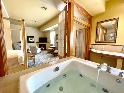 A luxurious hotel room featuring a jacuzzi, seating area, and a cozy fireplace in a warm, inviting atmosphere.