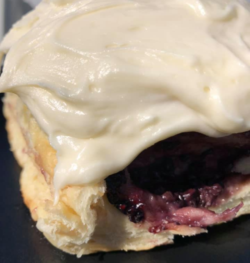 Close-up of a pastry filled with berry jam and topped with creamy frosting.