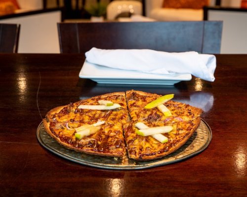 A pizza with caramelized onions and apple slices, served on a round metal tray, with a napkin in the background.