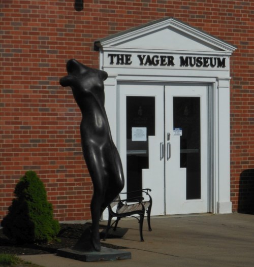 A sculpture of a figure stands outside the Yager Museum, with a brick building and entrance visible in the background.