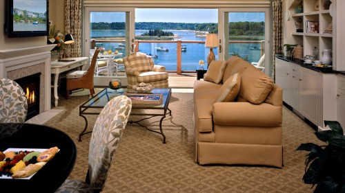 Cozy living room with a view of a lake, featuring a sofa, armchair, and a glass coffee table. Bright and inviting atmosphere.