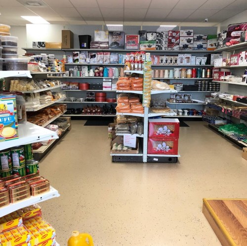 A well-stocked store aisle with shelves of various food items, kitchenware, and household products.