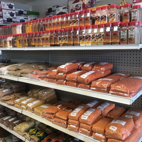 A grocery store shelf filled with various spices in jars and bags of lentils and grains neatly arranged.