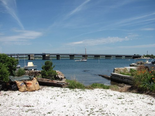 A scenic view of a bridge over water, with boats and greenery in the foreground under a clear blue sky.