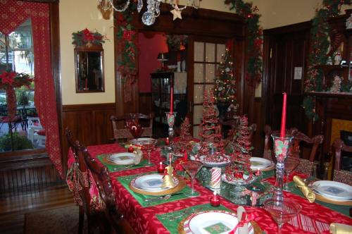 A festive dining room set for a holiday meal, decorated with red and green accents, candles, and a Christmas tree.