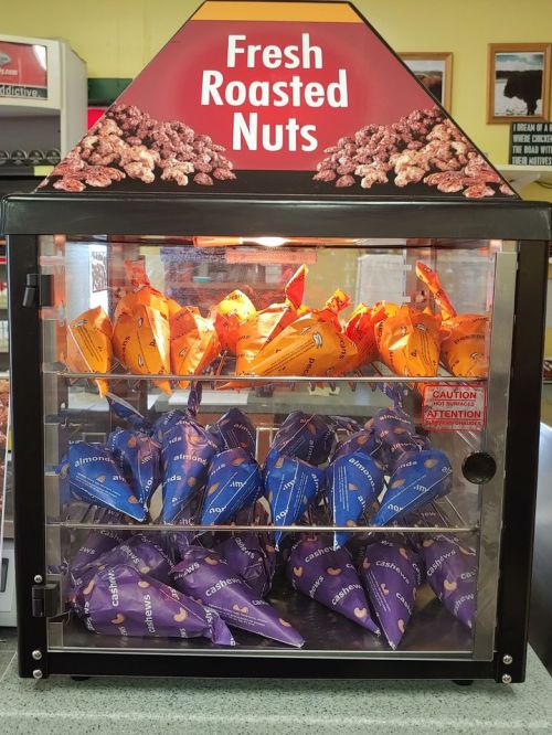 A display case filled with colorful bags of fresh roasted nuts, labeled with flavors like almonds and cashews.