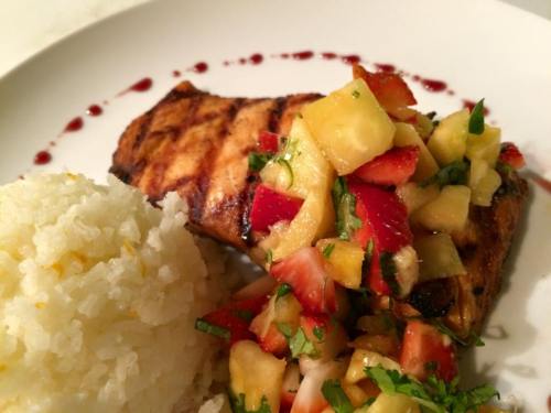 Grilled salmon topped with fresh fruit salsa, served with a side of fluffy white rice on a white plate.