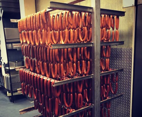 A metal rack filled with rows of hanging sausages in a commercial kitchen setting.