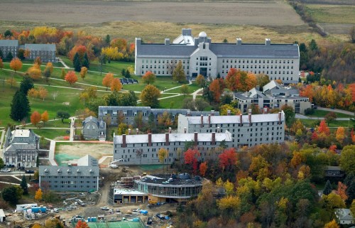 Aerial view of a campus with multiple buildings surrounded by colorful autumn trees and open fields.