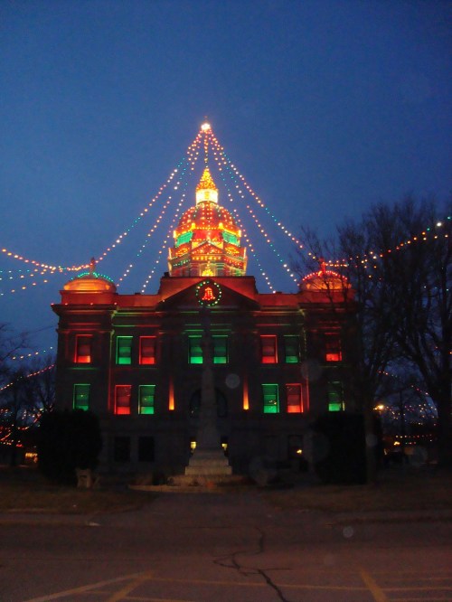 A historic building illuminated with colorful holiday lights against a twilight sky.