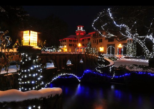 A snowy scene at night featuring a bridge adorned with blue and white lights, with a building illuminated in the background.
