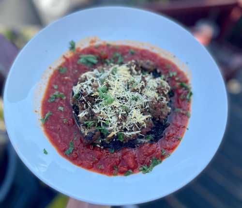 A plate of pasta topped with a rich meat sauce, garnished with herbs and grated cheese, served in a vibrant red sauce.