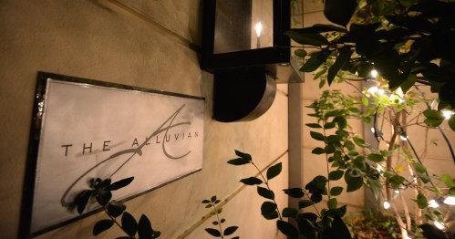 Sign for "The Alluvian" illuminated at night, surrounded by greenery and soft lighting.