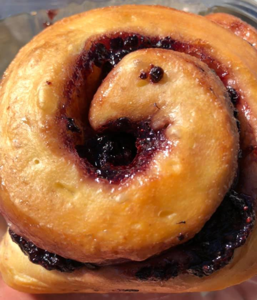 Close-up of a sweet roll with a glossy, jam-filled swirl, showcasing a golden-brown exterior and rich berry filling.
