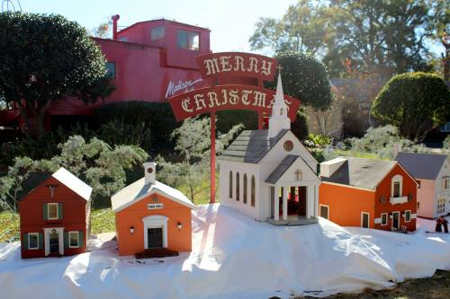 A festive display of miniature houses and a church with a "Merry Christmas" sign, set on a snowy landscape.