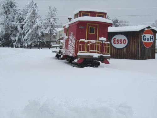 A red caboose and a wooden building with vintage gas station signs, surrounded by deep snow and winter scenery.