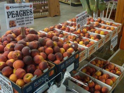 A display of Georgia peaches in various boxes, with price signs showing $44.99 for a 25 lb box and $2.49 per pound.