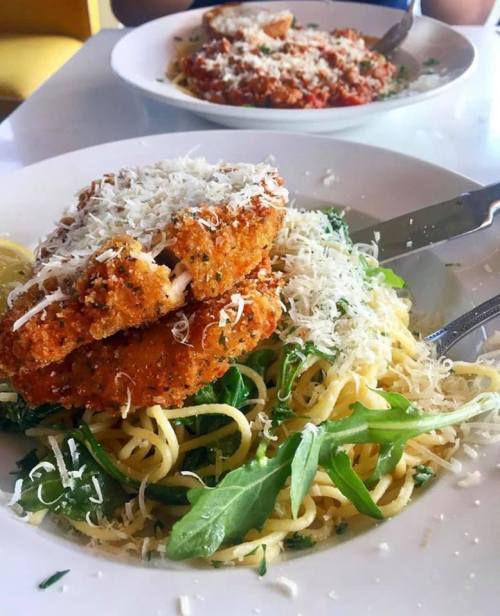 A plate of pasta topped with crispy chicken, arugula, and grated cheese, served with a side of marinara sauce.