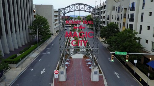 A large archway sign reading "Welcome to the Magic City" over a quiet street lined with buildings and greenery.