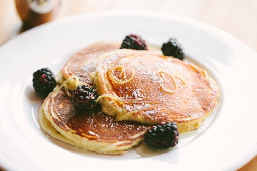 Three golden pancakes topped with powdered sugar and fresh blackberries on a white plate.