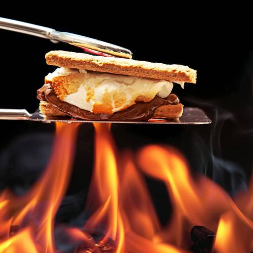 A s'more with chocolate and marshmallow on a spatula, held over a roaring fire.