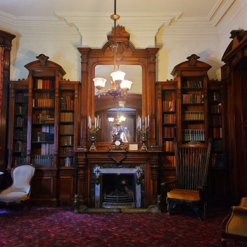 A cozy library with wooden bookshelves, a fireplace, and elegant furnishings, featuring warm lighting and rich decor.