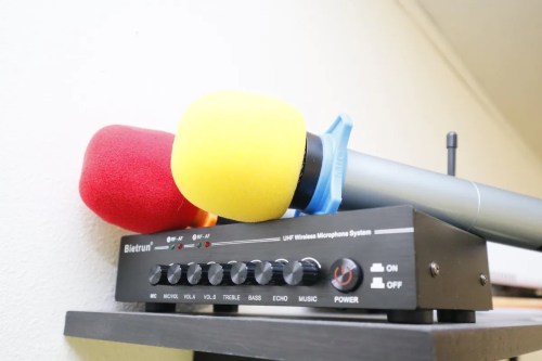 A wireless microphone system with red and yellow microphones on top, featuring volume and tone controls.