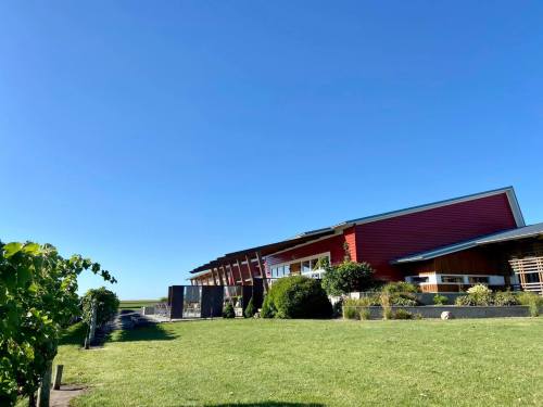 A red building with a modern design sits on a green lawn under a clear blue sky, surrounded by plants.