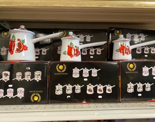 White cookware with floral designs displayed on shelves, alongside black boxes featuring similar kitchen items.