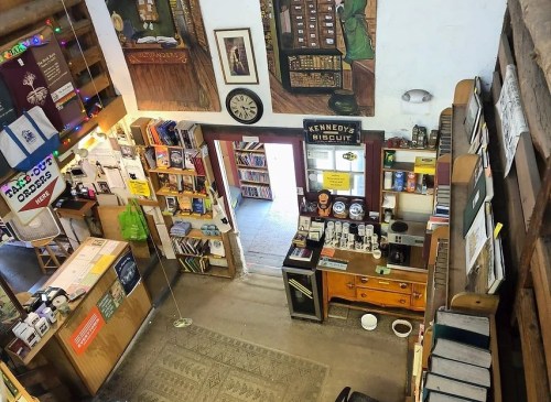 A cozy bookstore interior with wooden shelves, a counter, and colorful decorations, viewed from above.