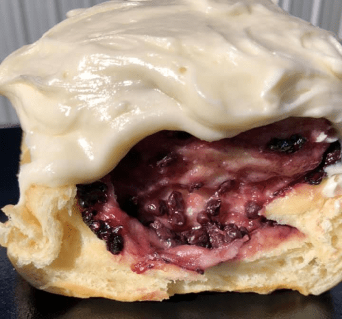 A close-up of a cinnamon roll with cream cheese frosting, revealing a berry filling inside.