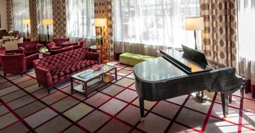 A stylish lounge with a grand piano, plush seating, and large windows letting in natural light.
